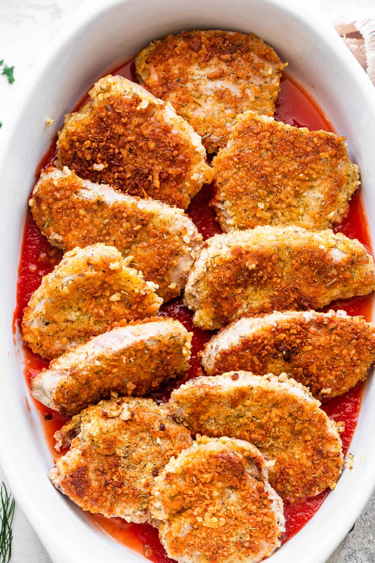 breaded pork medallions arranged in a white baking dish