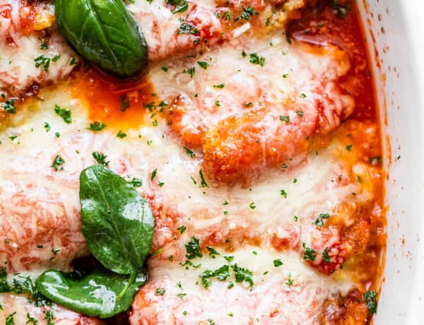 close up overhead shot of baked pork parmigiana topped with melted cheese and basil leaves.