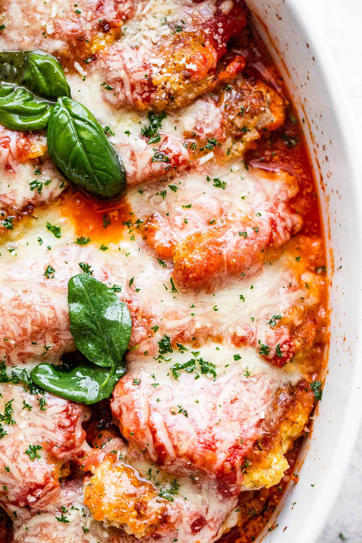 close up overhead shot of baked pork parmigiana topped with melted cheese and basil leaves.