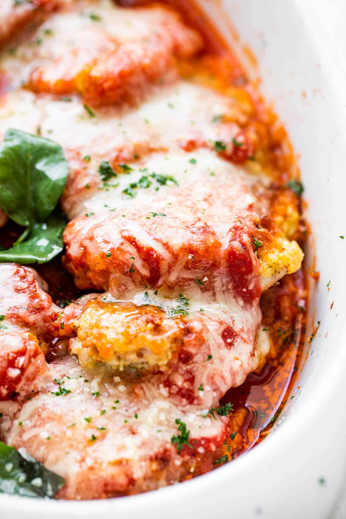 close up side shot of baked pork parmigiana topped with melted cheese and basil leaves.