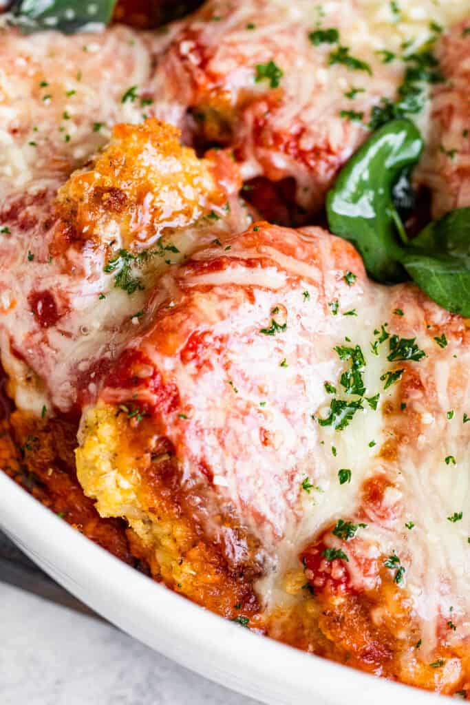 close up shot of baked pork parmigiana topped with melted cheese and basil leaves.