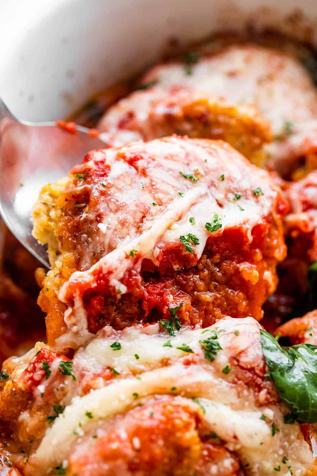 spooning out baked pork parmigiana medallions from baking dish.