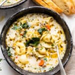 overhead shot of creamy tortellini sausage soup in a black soup bowl with a spoon inside