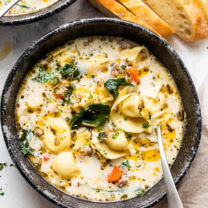 overhead shot of creamy tortellini sausage soup in a black soup bowl with a spoon inside