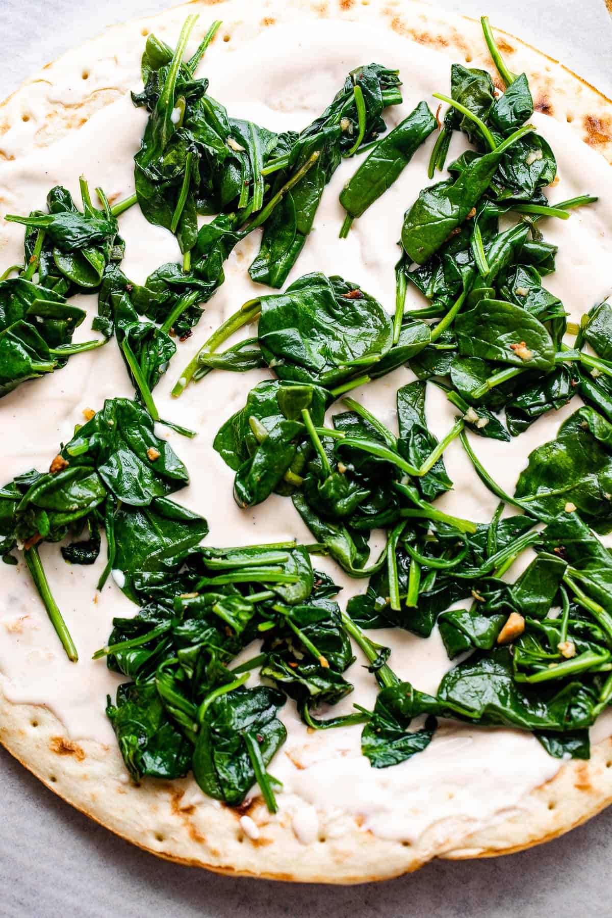 pizza crust topped with alfredo sauce and baby spinach