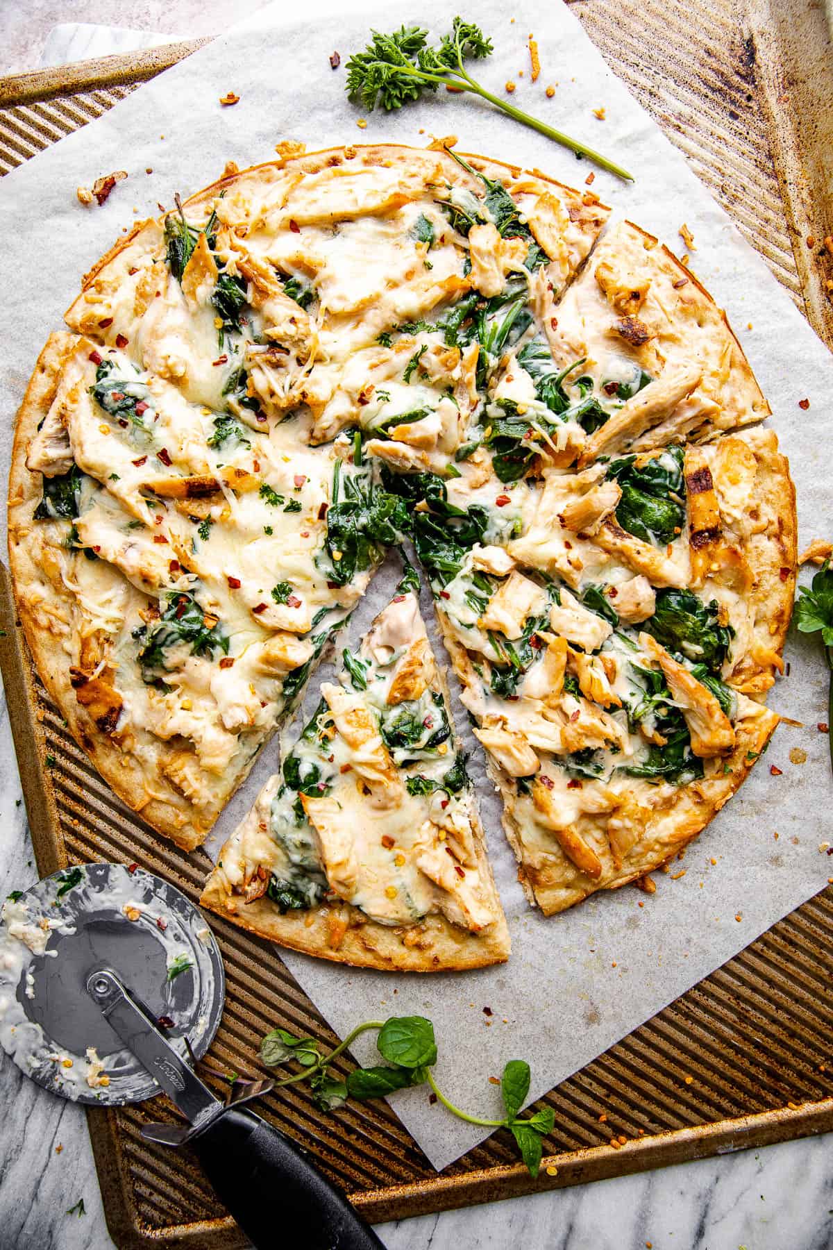 overhead shot of homemade chicken alfredo pizza with pizza cutter placed next to the pizza