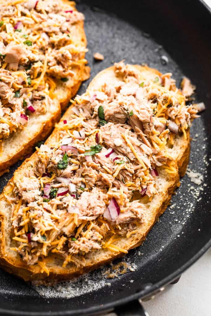 bread slices topped with flaked tuna and cooking in a black skillet