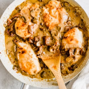Chicken in a creamy marsala sauce with a wooden serving spoon.