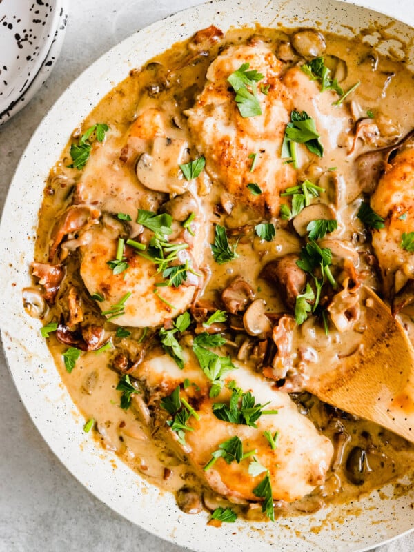 Chicken marsala in a white pan with a wooden spoon