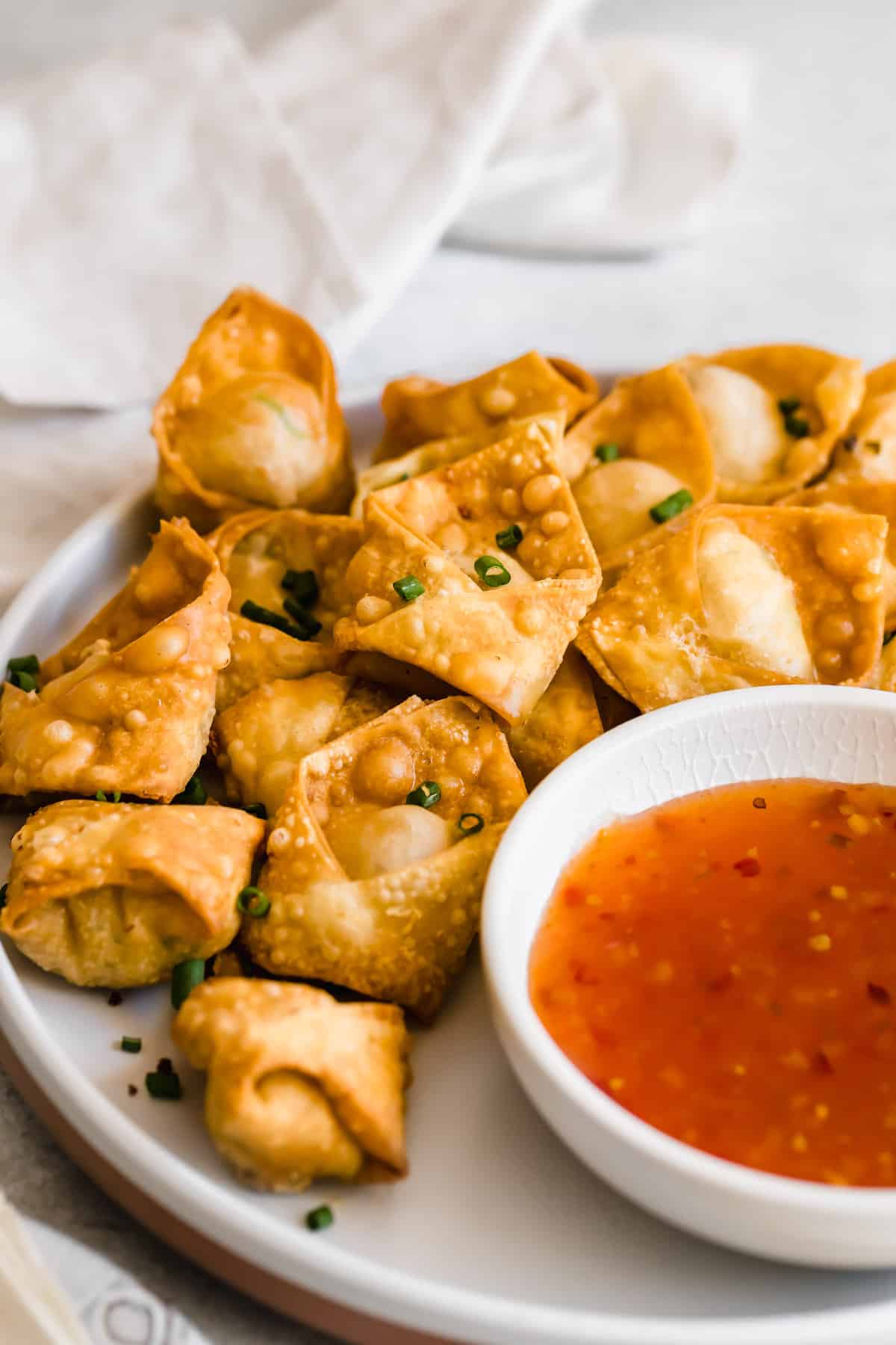 Crab rangoons on a white plate served with dipping sauce.