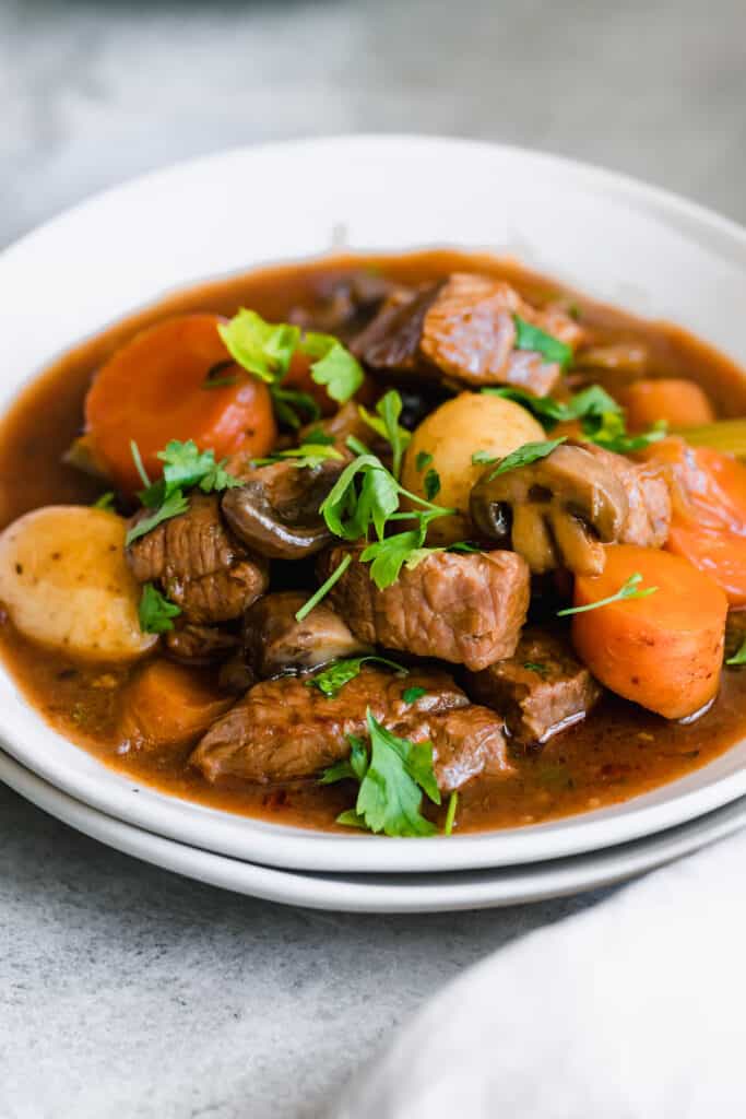 A white bowl of Guinness Beef Stew with carrots and potatoes with fresh herbs.