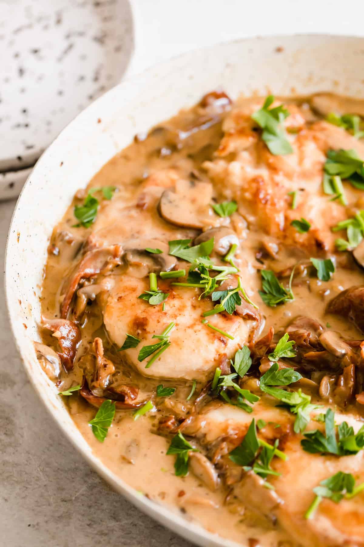 Creamy chicken marsala in a white bowl sprinkled with herbs.