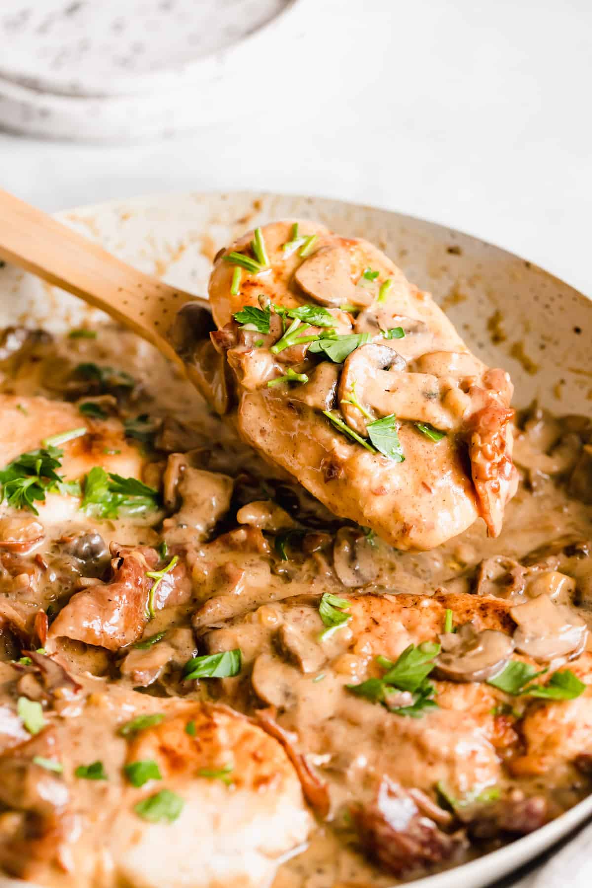 A piece of chicken in creamy marsala sauce on a wooden serving spoon.