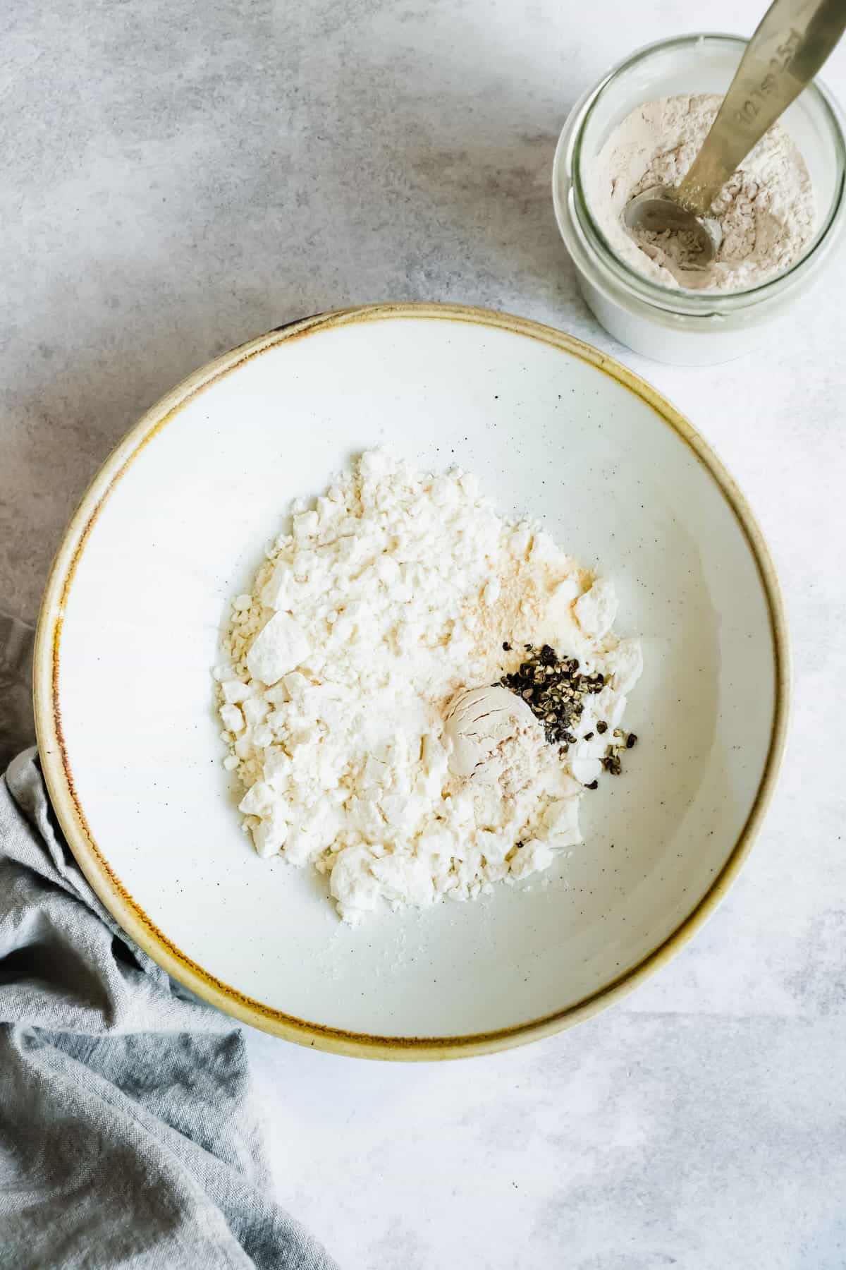 A white bowl of flour with crushed black pepper.