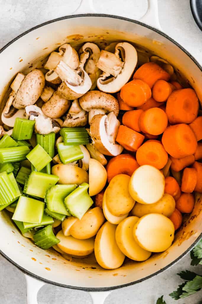 Chopped raw celery, carrots, onions, potatoes, and mushrooms in a soup pot.