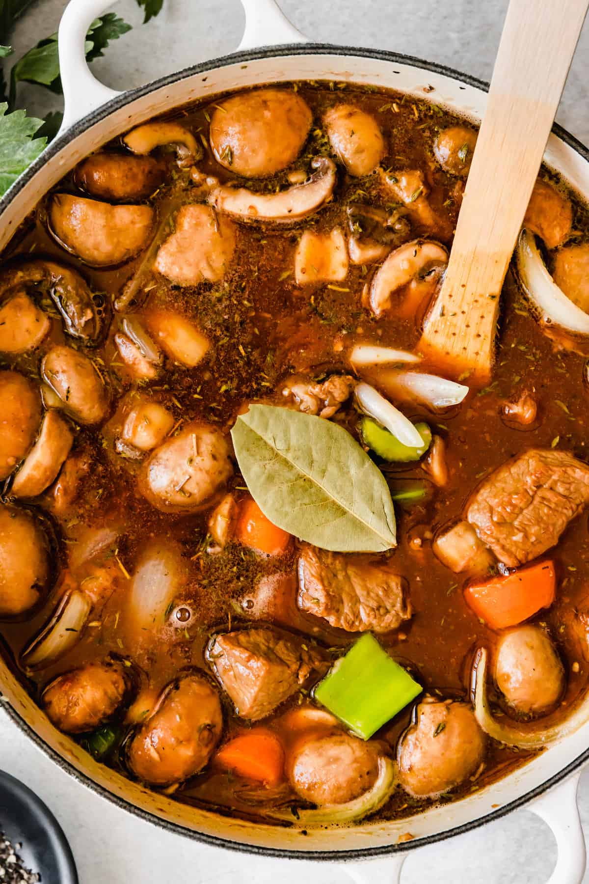 Beef stew cooking with a fresh bay leaf on top.