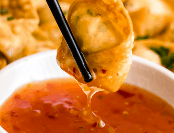 holding chopsticks and dipping crab rangoon wonton in dipping sauce