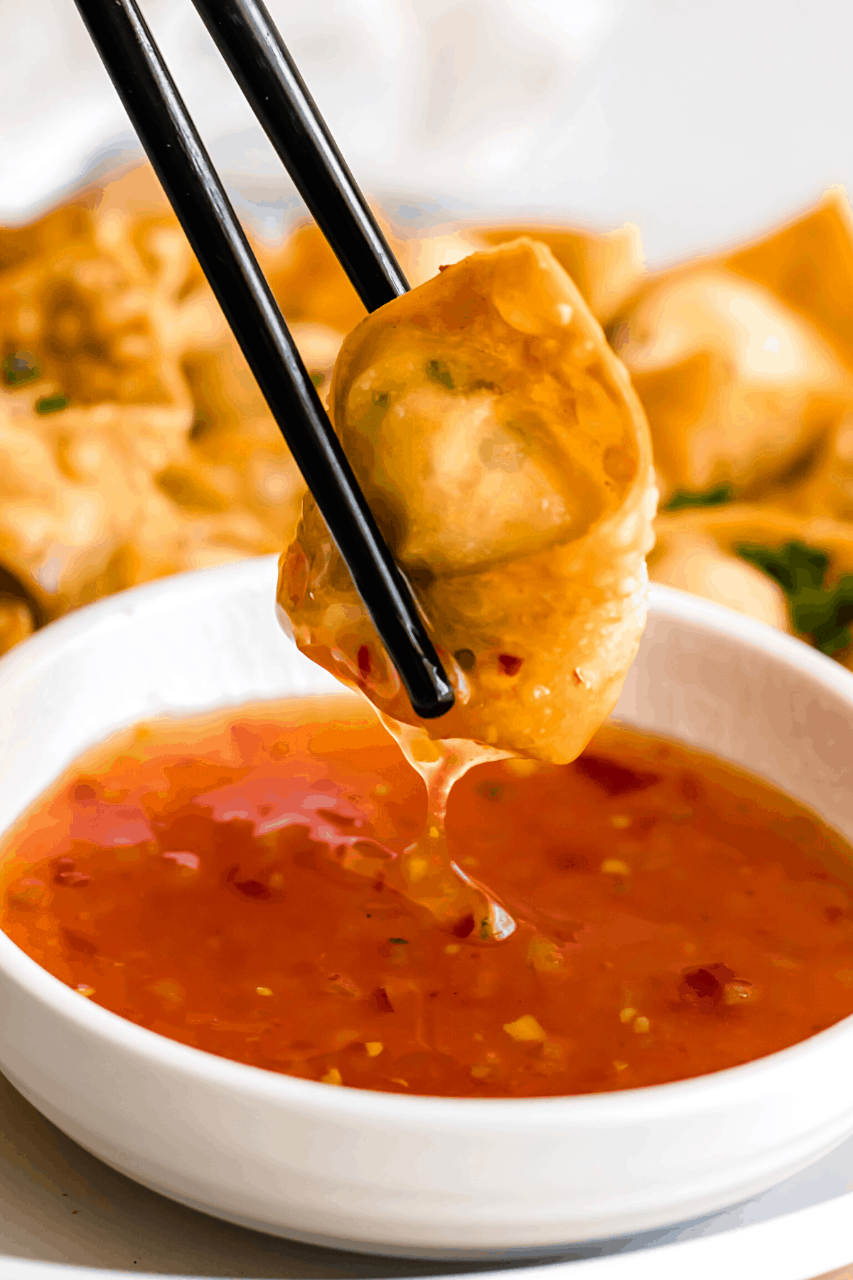 holding chopsticks and dipping crab rangoon wonton in dipping sauce