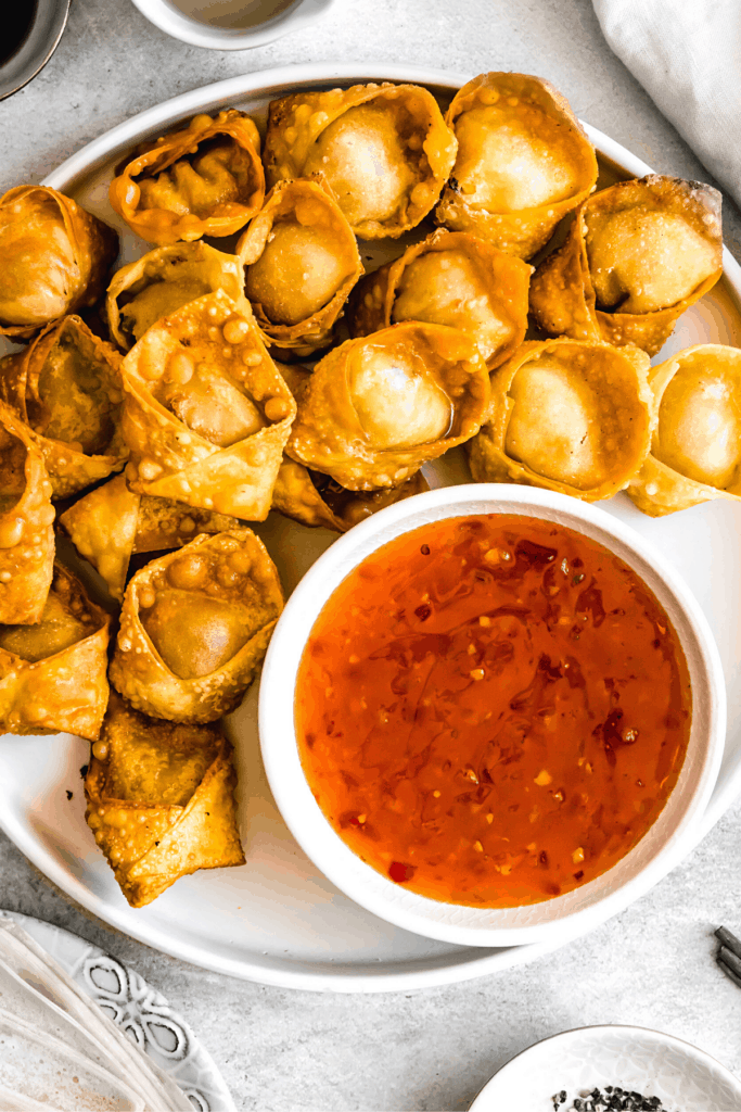 crab rangoon wontons arranged on a plate with a dipping sauce