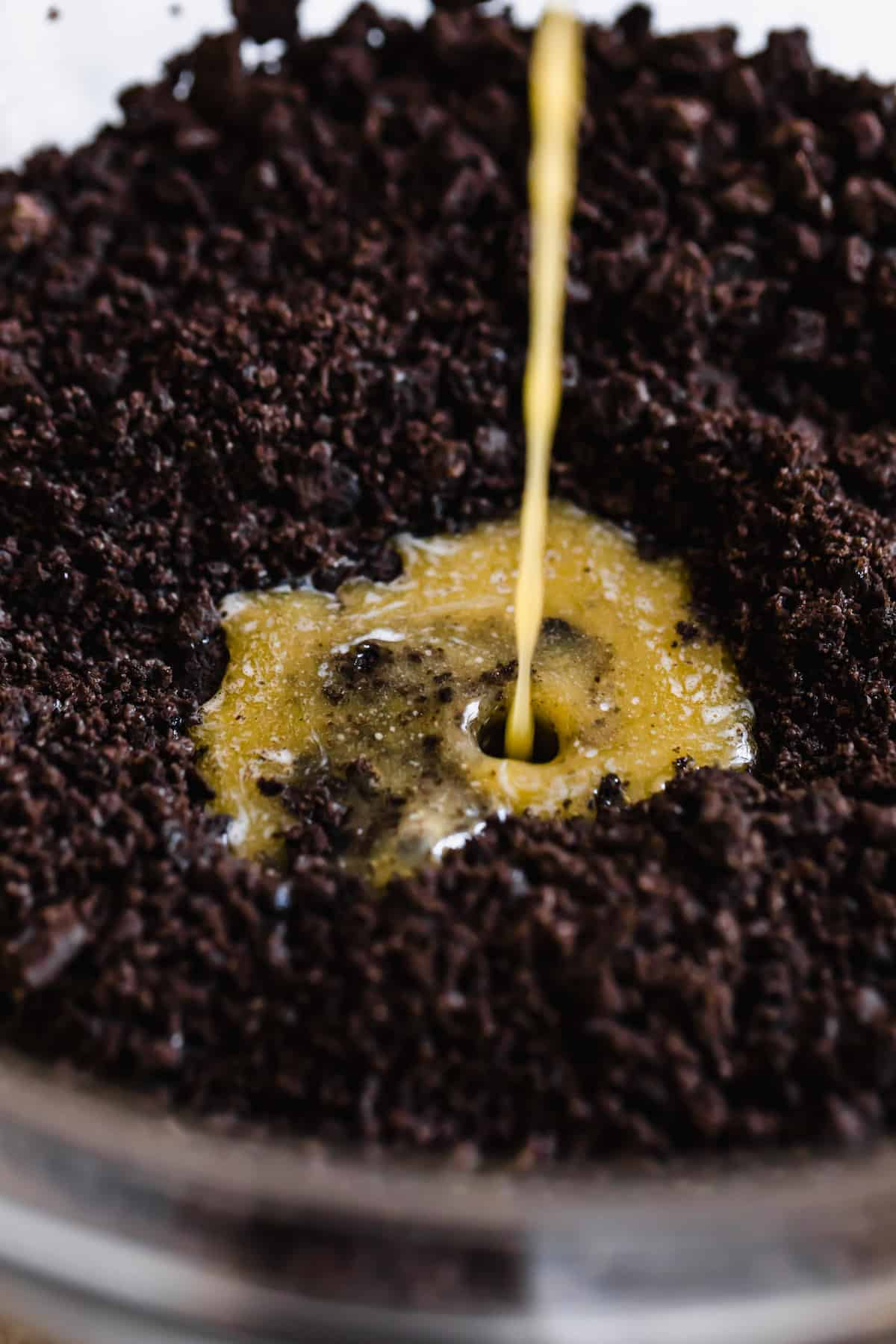 Melted Butter Being Poured into a Bowl of Oreo Cookie Crumbs