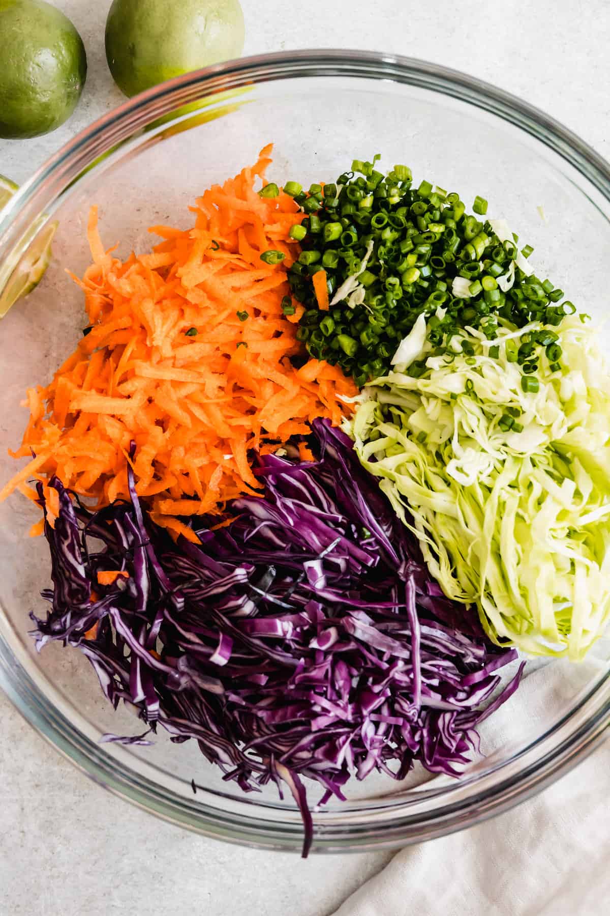 A Bowl Filled with the Cabbage Slaw Ingredients Beside Two Limes and Half of Another Lime