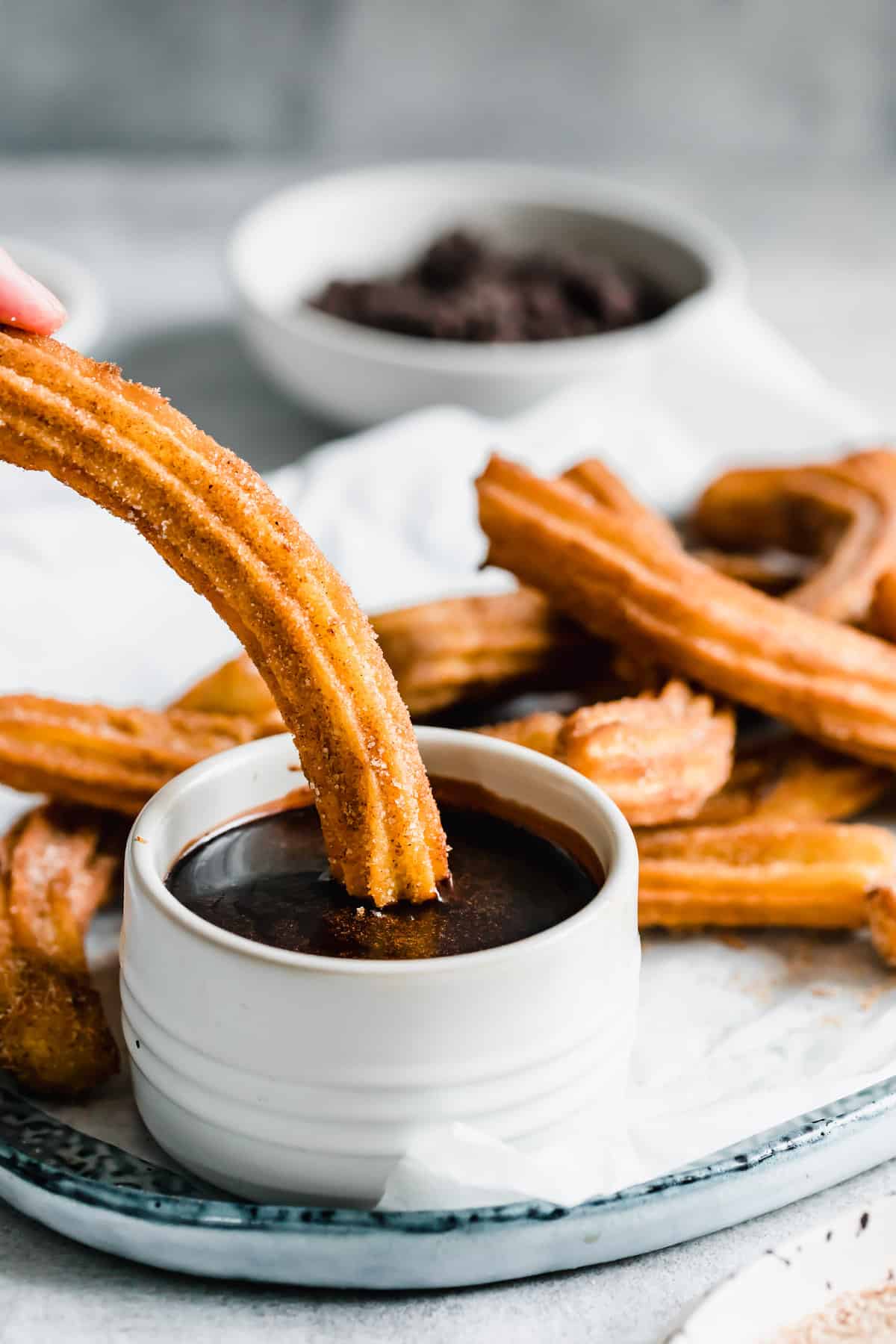 A Hand Dunking a Churro Into the Chocolate Dipping Sauce