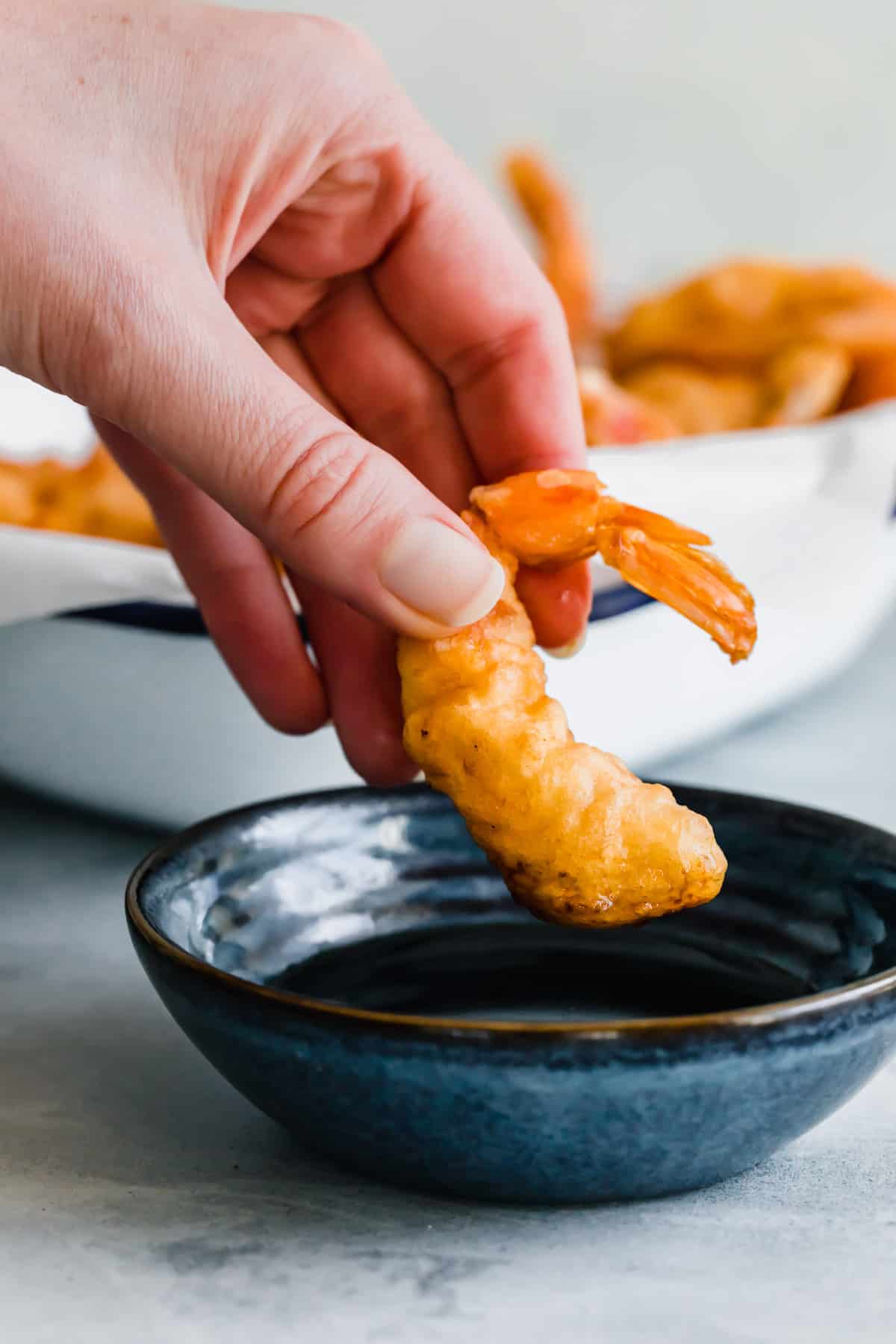 A Hand Dunking a Pan-Fried Shrimp Into a Bowl of Dipping Sauce
