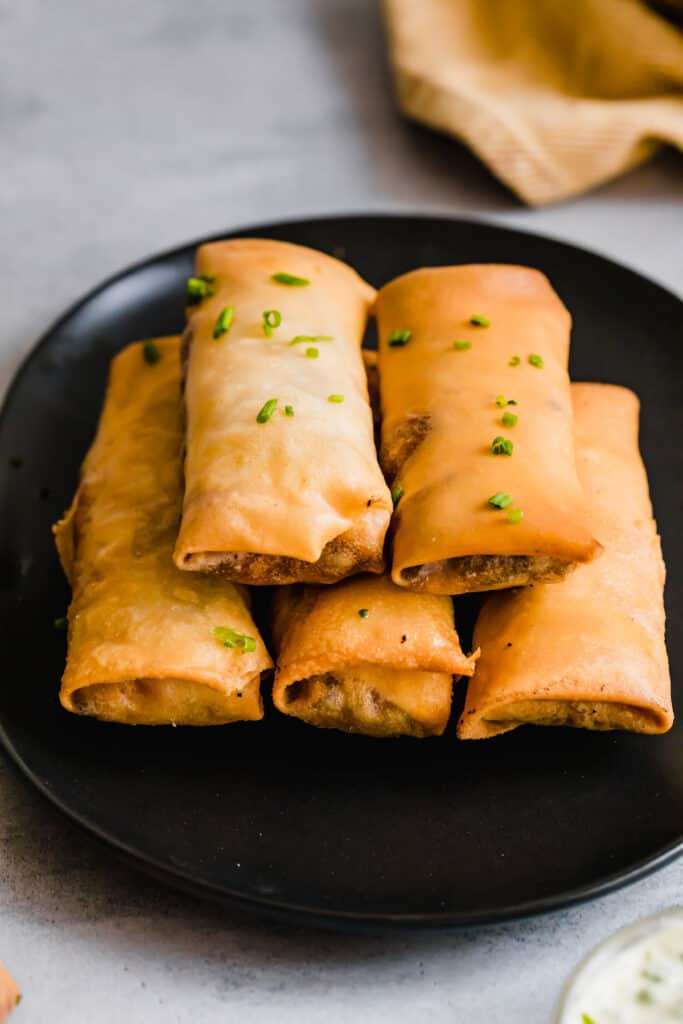 Five Egg Rolls Piled Neatly on a Shiny Black Plate