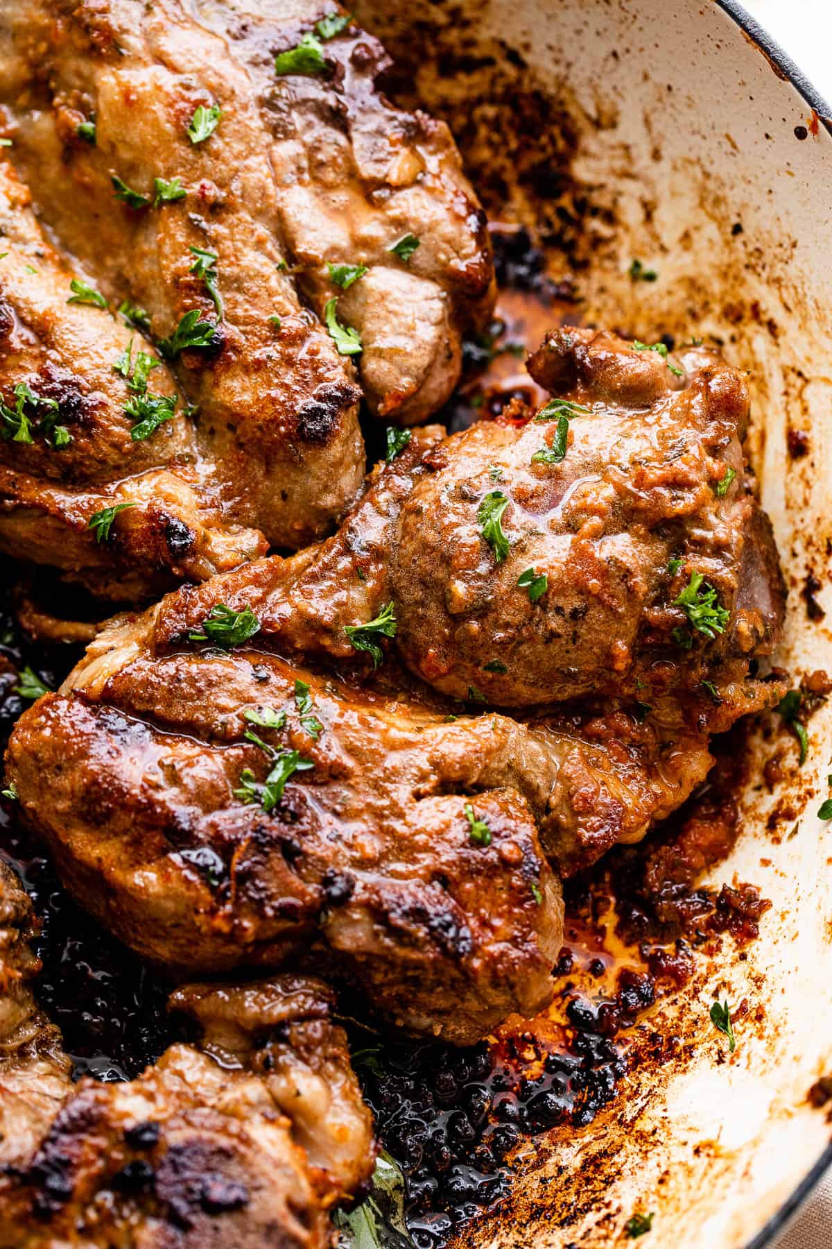 close up of lamb shoulder chops cooking in a white cast iron skillet