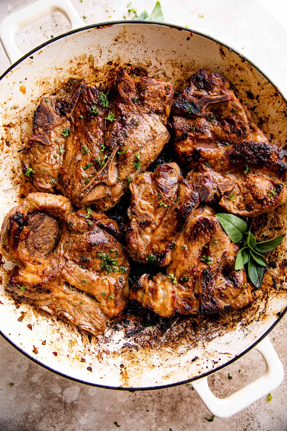 overhead shot of a white cast iron skillet with cooked lamb chops inside