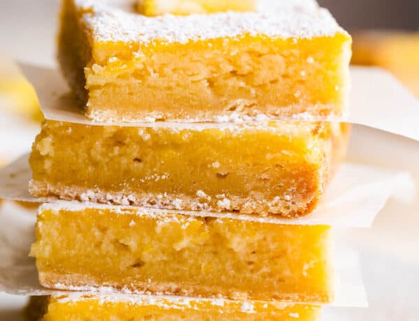 four lemon bars stacked one on top of the other and finished with a dusting of powdered sugar and a slice of lemon on top