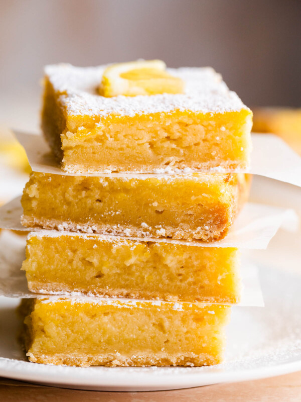 four lemon bars stacked one on top of the other and finished with a dusting of powdered sugar and a slice of lemon on top