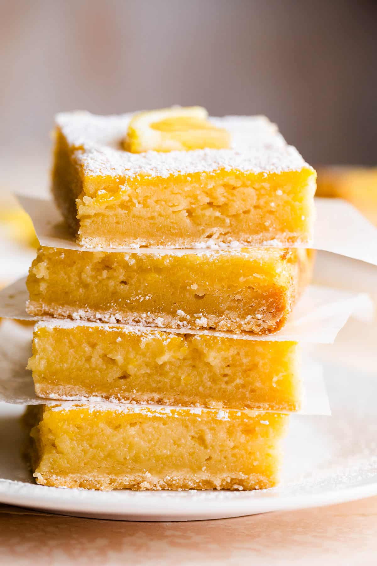 four lemon bars stacked one on top of the other and finished with a dusting of powdered sugar and a slice of lemon on top