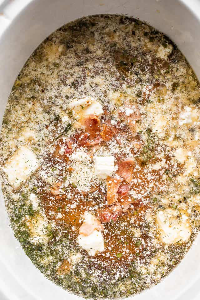chicken broth, cubed cream cheese, bacon, chicken breasts, and seasonings inside the insert of a slow cooker