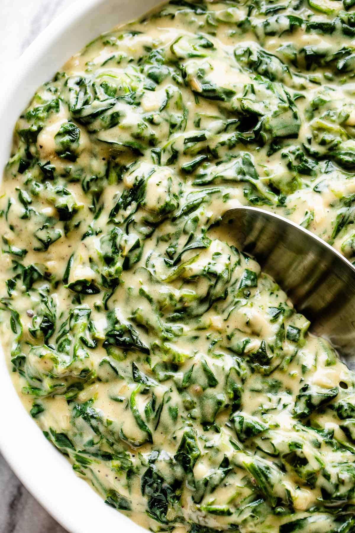 served creamed spinach in a white bowl with spoon inside