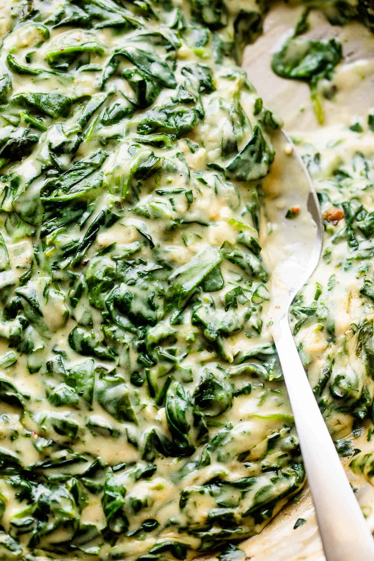 Stirring creamed spinach with a large spoon.