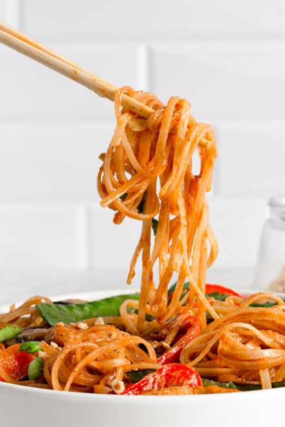 A Pair of Chopsticks Holding a Bite of Chicken Lo Mein Over the Bowl