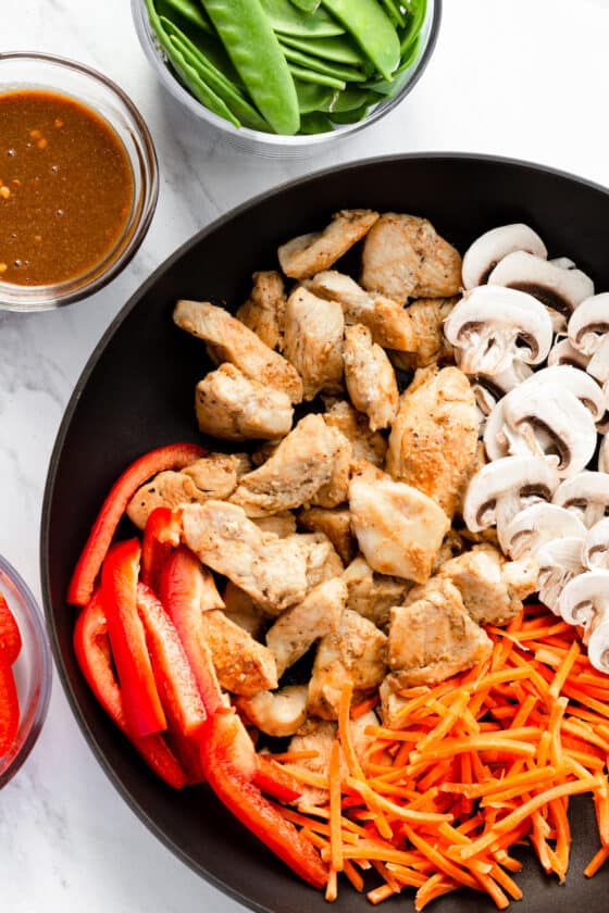 Cooked Chicken, Shredded Carrots, Mushrooms and Red Pepper Slices in a Skillet Beside the Other Ingredients