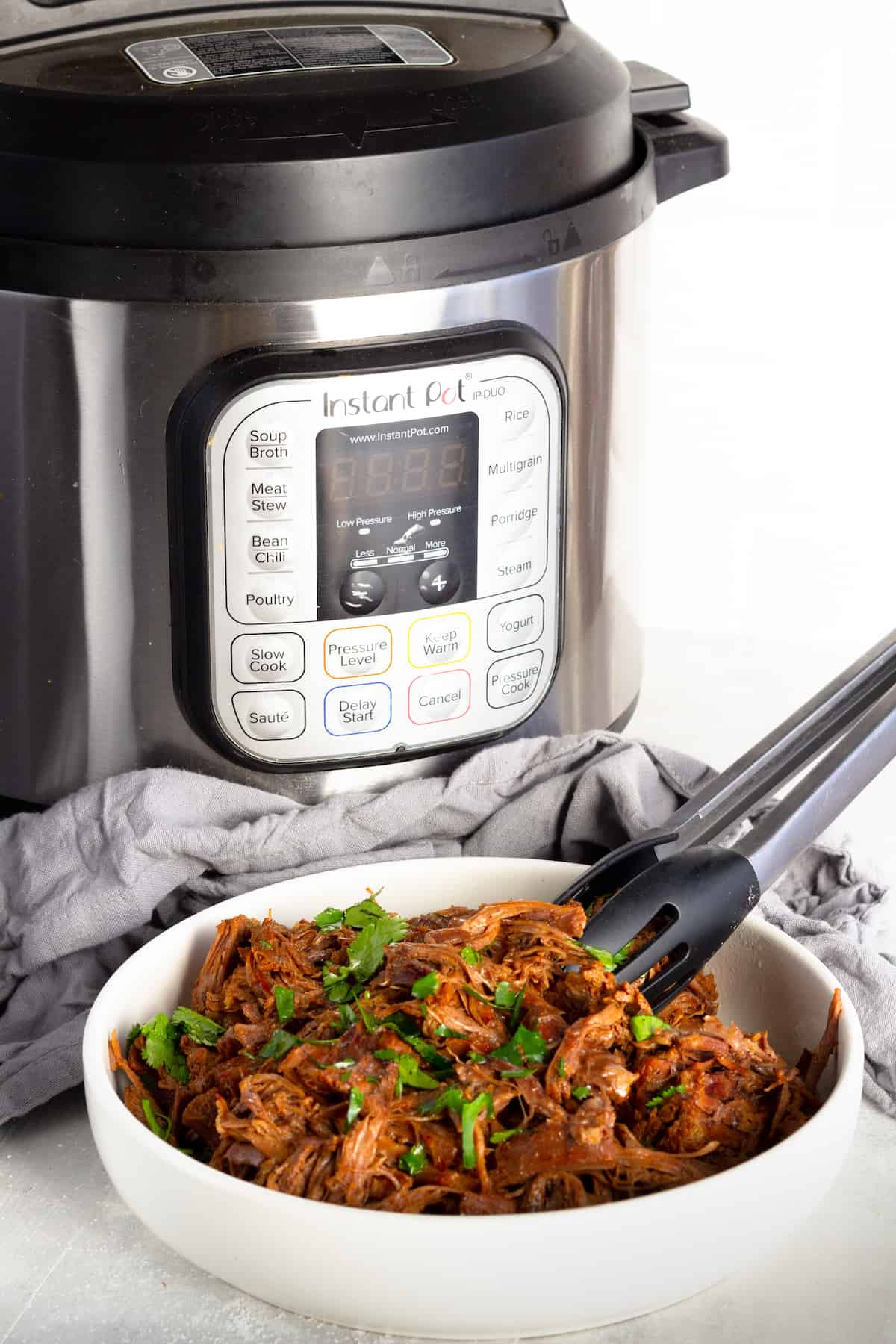 A Bowl of Beef Barbacoa in Front of an Instant Pot and a Gray Kitchen Towel