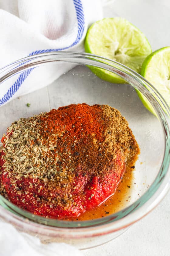 The Tomato Paste, Seasoning and Lime Juice Mixture in a Glass Bowl Beside a Juiced Lime
