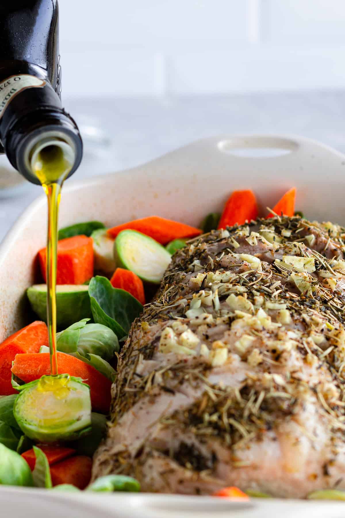 This easy pork loin roast is juicy, tender, and seasoned with garlic and herbs. Roasted with potatoes, carrots, and celery, it’s a complete one-pan dinner. Olive Oil Being Drizzled Over the Raw Veggies in the Casserole Dish