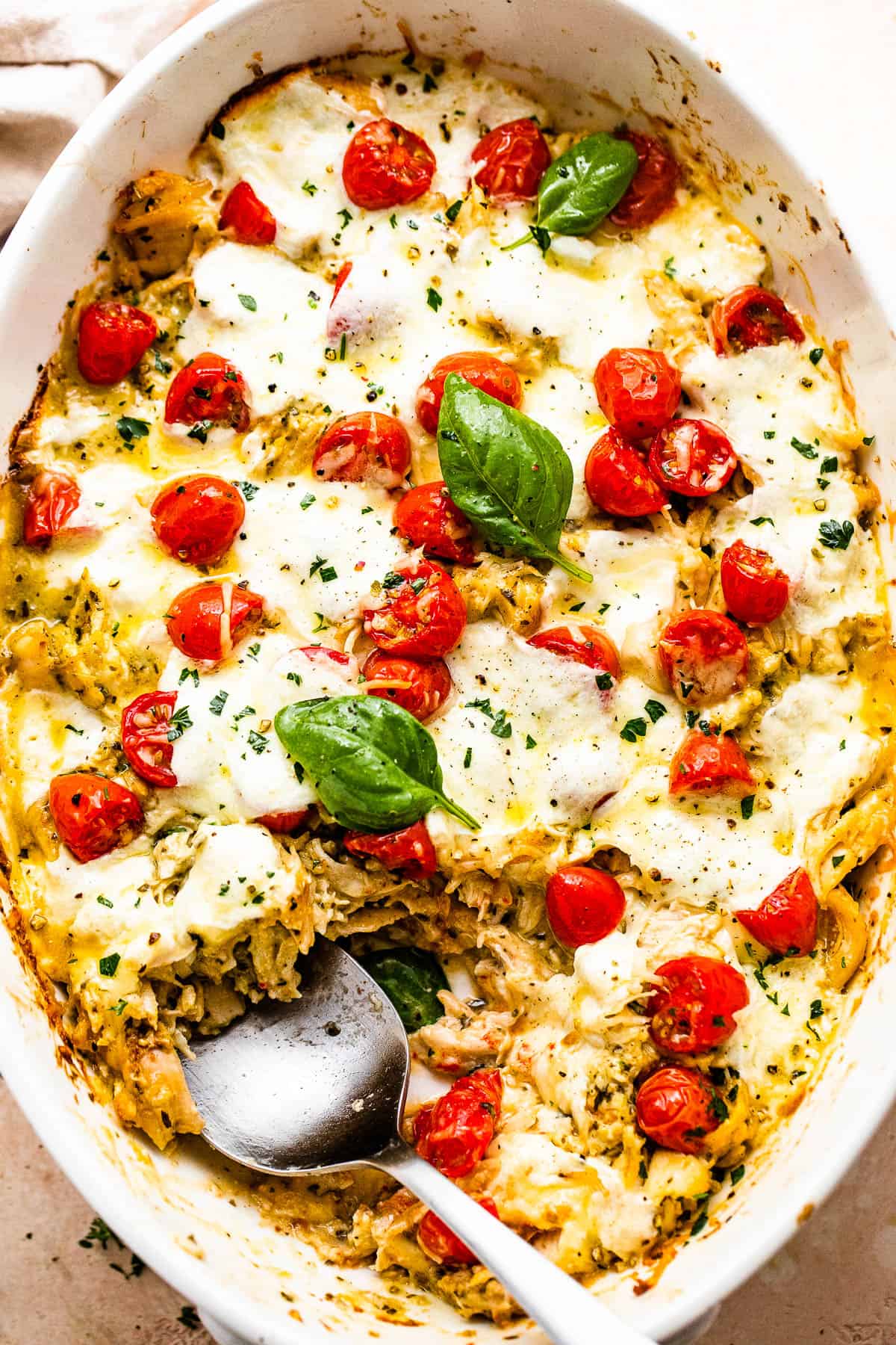 spooning out chicken caprese casserole from the baking dish