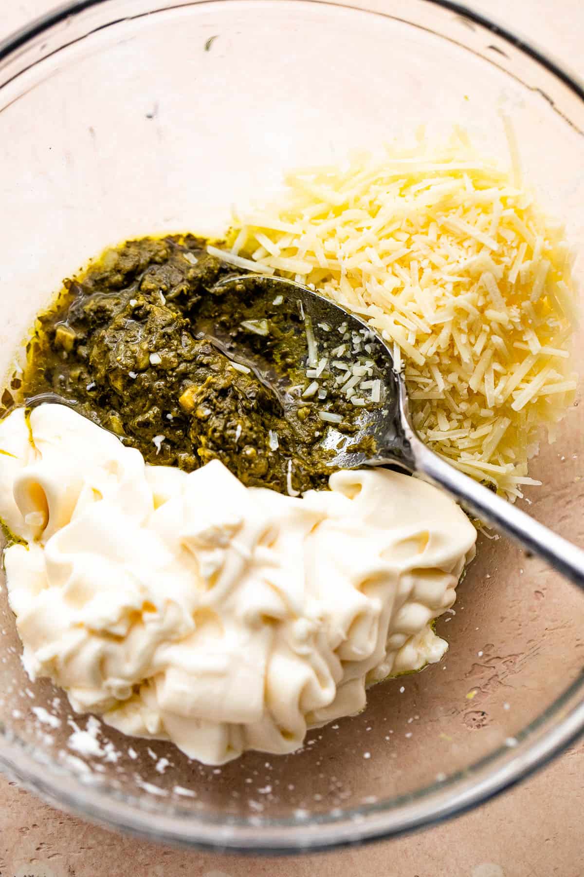 mixing together basil pesto, mayonnaise, and parmesan cheese