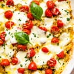 chicken caprese casserole in a white baking dish topped with basil leaves and cherry tomatoes