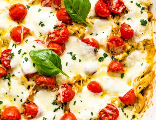 chicken caprese casserole in a white baking dish topped with basil leaves and cherry tomatoes