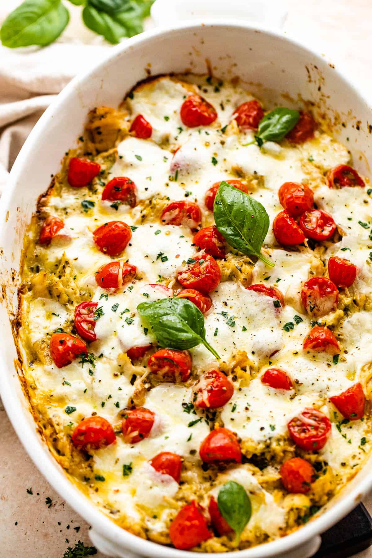chicken caprese casserole in a white baking dish topped with basil leaves and cherry tomatoes