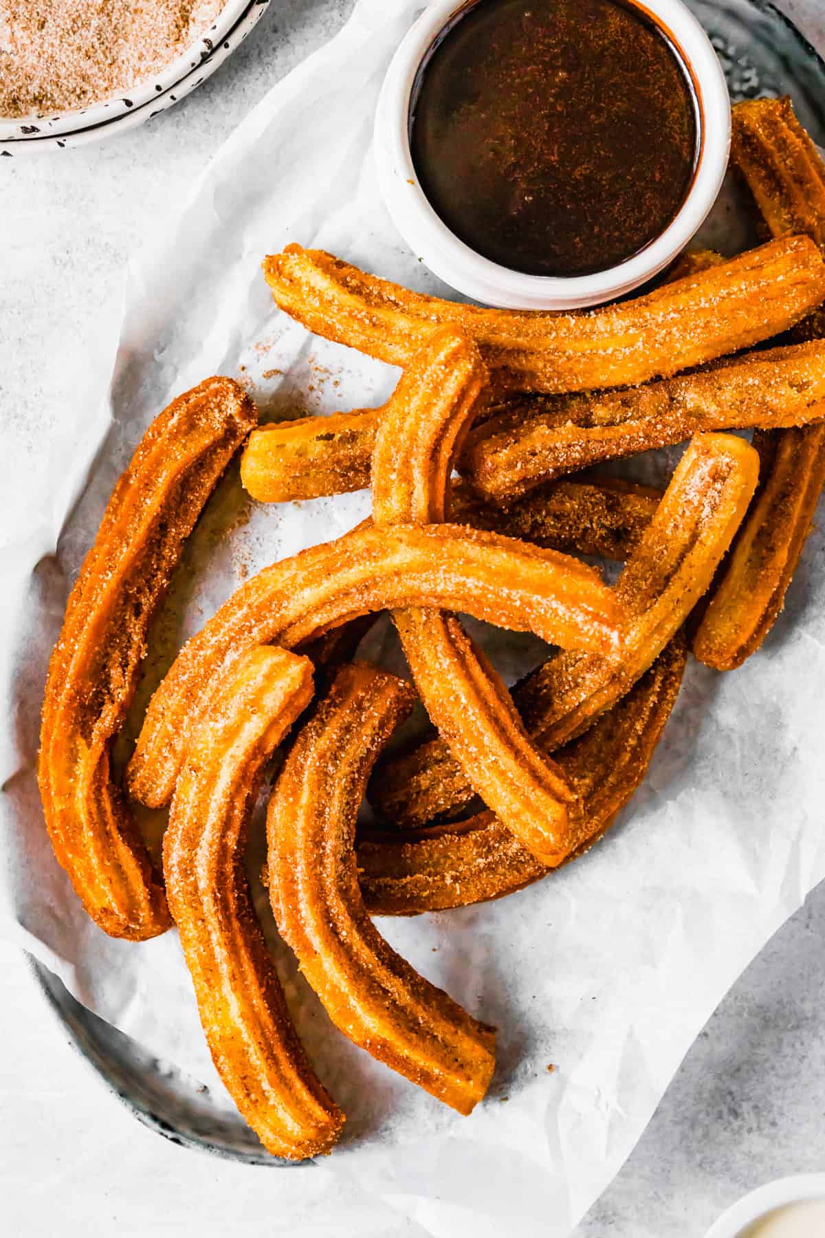 Churros recipe by easy weeknight recipes. The churros are served on a plate with a bowl of chocolate sauce.