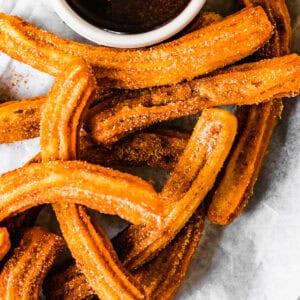 Churros recipe by easy weeknight recipes. The churros are served on a plate with a bowl of chocolate sauce.