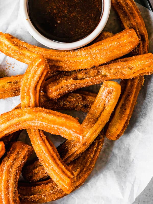 Churros recipe by easy weeknight recipes. The churros are served on a plate with a bowl of chocolate sauce.
