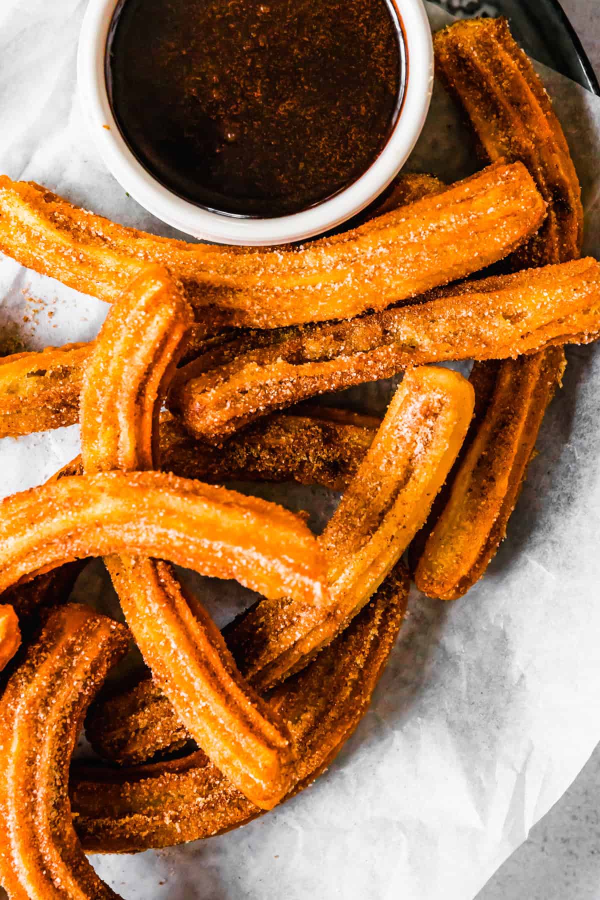 Churros recipe by easy weeknight recipes. The churros are served on a plate with a bowl of chocolate sauce.